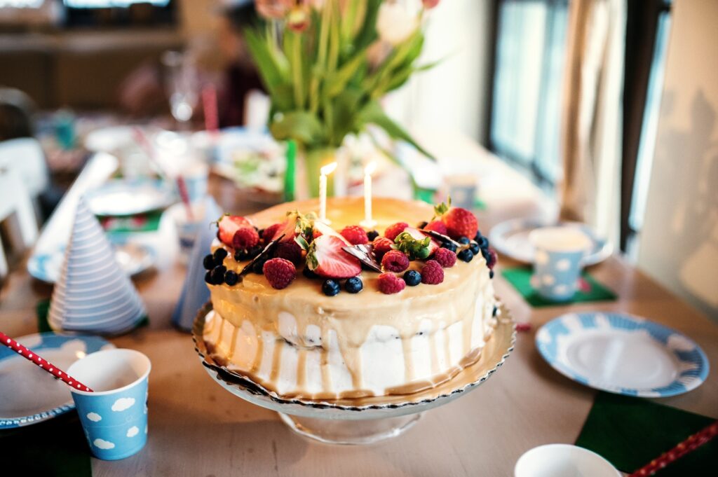 A birthday cake on a glass stand and a vase with tulips on the table.